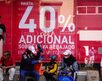 personas con bolsas de compras esperan afuera de una tienda con un anuncio del buen fin