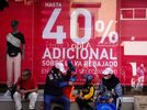 personas con bolsas de compras esperan afuera de una tienda con un anuncio del buen fin