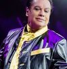 Juan Gabriel en un concierto abriendo los brazos y sosteniendo el micrófono. juan Gabriel aparece vestido de negro con dorado.