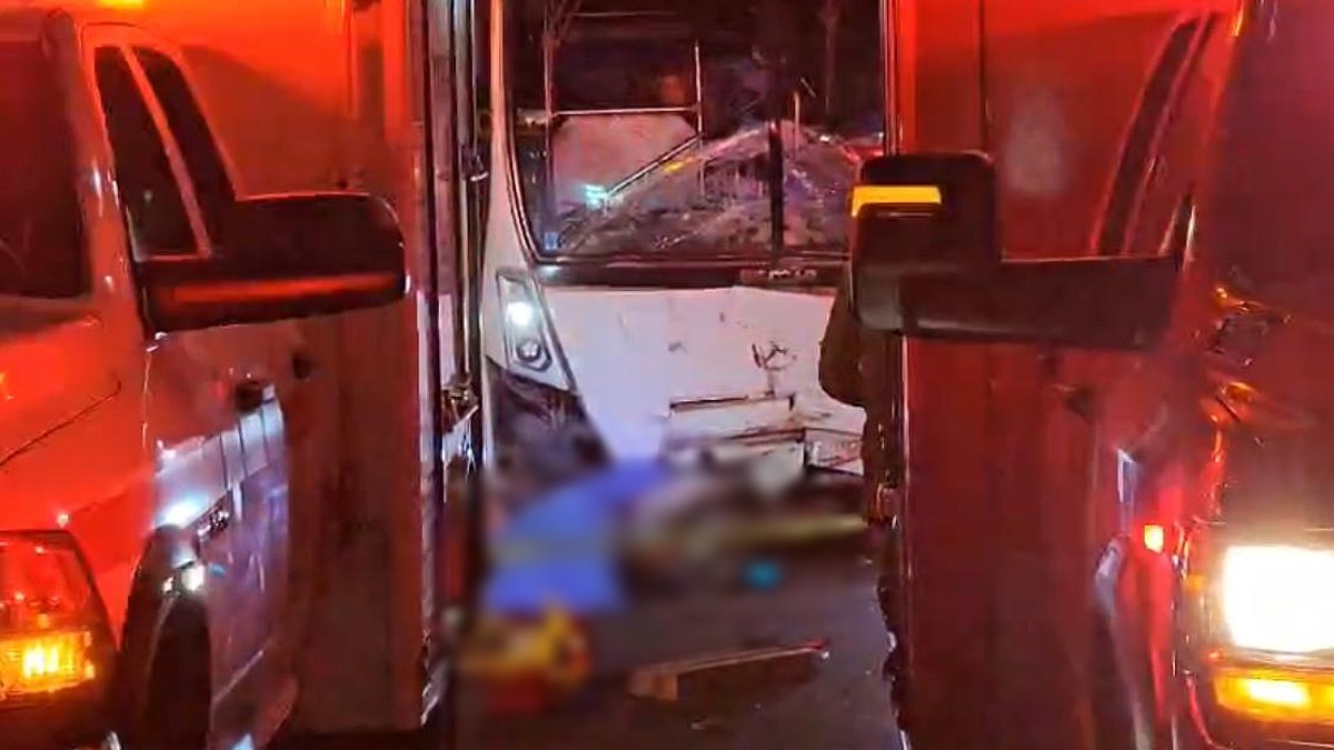 motocicleta tumbada sobre el asfalto y cubierta con una manta azul enfrente de un camión de transporte con el vidrio roto y en medio de dos vehículos