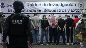 Oficial de la UECS Jalisco de espaldas con los siete hombres detenidos también de espaldas y miembros del ejército a los lados