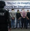 Oficial de la UECS Jalisco de espaldas con los siete hombres detenidos también de espaldas y miembros del ejército a los lados