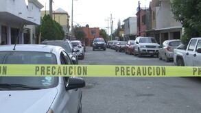 Hay carros estacionados y una cinta de precaución amarilla, además al fondo se encuentra una patrulla.