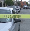 Hay carros estacionados y una cinta de precaución amarilla, además al fondo se encuentra una patrulla.