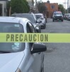Hay carros estacionados y una cinta de precaución amarilla, además al fondo se encuentra una patrulla.