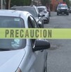 Hay carros estacionados y una cinta de precaución amarilla, además al fondo se encuentra una patrulla.