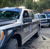 Primer plano de una camioneta de la Policía de Guadalajara estacionada en la calle, con otra patrulla detrás. Al fondo se distingue un área de juegos mecánicos