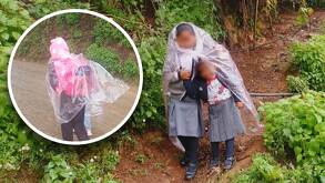 Niños con uniforme escolar se cubren de la lluvia con plásticos.
