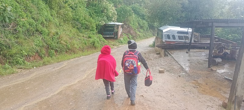 Niños con uniforme escolar y cubiertos para evitar el frío avanzan en un camino de tierra.
