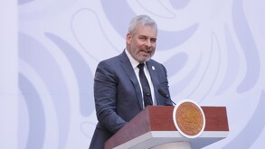 El Gobernador de Michoacán, Alfredo Ramírez Bedolla, viste un traje oscuro y habla ante un gran micrófono. En un círculo insertado se ve al político