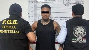 Hombre tatuado y que viste playera negra siendo detenido por sujetos vestidos de negro.