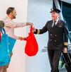 Pilotos de avión saludan y reciben bolsas de regalo rojas y azules de un promotor en la pasarela de un aeropuerto. Esto probablemente marca la inauguración de n