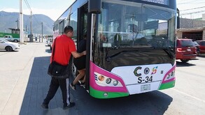 Un hombre quien viste una playera roja se está subiendo a una ruta de transporte.