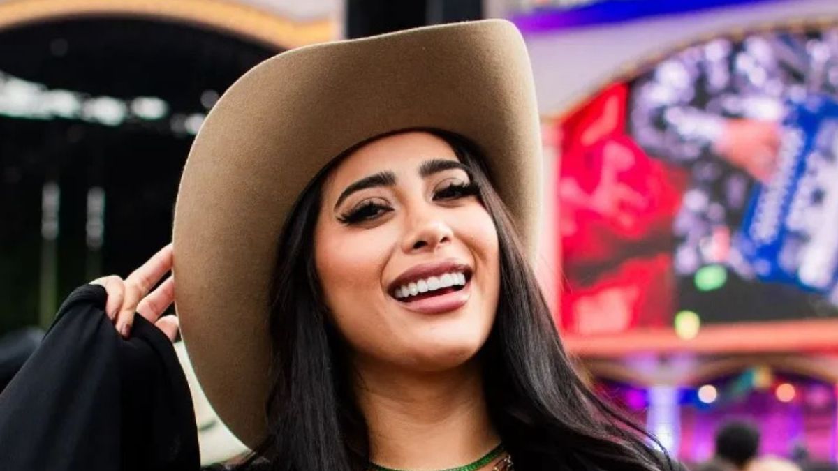 Kim Shantal sonriendo y posando para la foto, portando un sombrero color cafe y de fondo se puede ver que se encuentra en un festival de música.