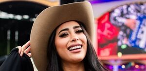 Kim Shantal sonriendo y posando para la foto, portando un sombrero color cafe y de fondo se puede ver que se encuentra en un festival de música.