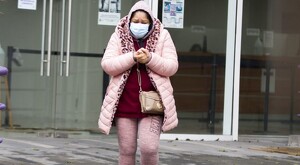 Mujer caminando con abrigo rosa y cubrebocas mientras se frota las manos debido al frío en las calles de Guadalajara