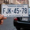 Unas placas con las letras FJK-45-78 y detrás se ve un automóvil en la ciudad de Saltillo, ya que al fondo se ve la Catedral.