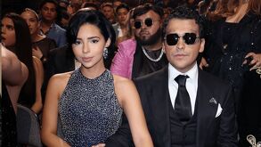 Ángela Aguilar y Christian Nodal juntos en una entrega de premios. Ángela luciendo un vestido negro con diamantes en plateado y Nodal con lentes oscuros.