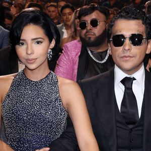 Ángela Aguilar y Christian Nodal juntos en una entrega de premios. Ángela luciendo un vestido negro con diamantes en plateado y Nodal con lentes oscuros.
