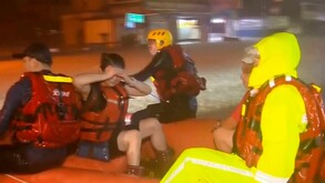 Rescatistas con chalecos salvavidas y ropa impermeable están en un bote inflable naranja en la noche, posiblemente durante una inundación en Taiwán. Uno de los