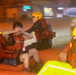 Rescatistas con chalecos salvavidas y ropa impermeable están en un bote inflable naranja en la noche, posiblemente durante una inundación en Taiwán. Uno de los