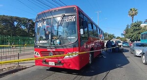 Vista de frente del camión de la ruta 604 de Guadalajara de color rojo detrás de una cinta policiaca sobre la vía pública con autos alrededor