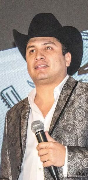 Julión Álvarez con sombrero negro y saco en color gris, además una imagen de sus pies pisando un celular.