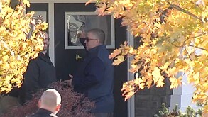 Dos hombre afuera de una casa frente a dos árboles