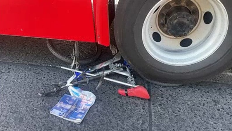Bicicleta sobre el pavimento con bolsa amarrada y debajo de la llanta de un camión de la ruta 604 de color rojo en Guadalajara