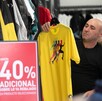 Hombre calvo sostiene una playera amarilla en oferta en una tienda de ropa.