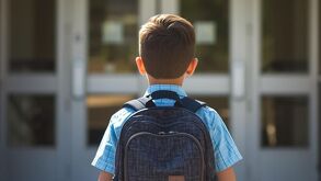 Niño de espaldas con su mochila, observando las puertas cerradas de una escuela.