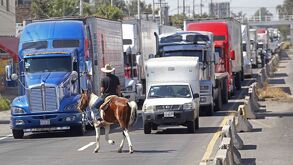 Hombre montado a caballo pasa frente a una autopista con vehículos detenidos.