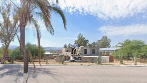 Carretera rodeada de casas, una palma y de fondo el cielo azul con nubes blancas
