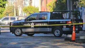 Vista lateral de una Patrulla de la Policía Municipal de Guadalajara estacionada sobre la calle y detrás de una cinta policiaca