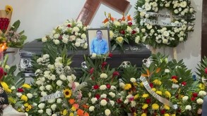 Ataúd en color gris rodeado de flores de color verde, blanco y amarillo