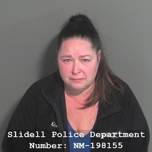 Mujer con coleta alta vistiendo sudadera negra y blusa azul viendo de frente con un fondo gris de la estación de policía