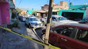 Patrulla de la Policía de Tlaquepaque estacionada fuera de la casa donde fue asesinada la joven con autos alrededor y una cinta policiaca puesta.