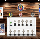 Un gabinete de trofeos del Club Deportivo Guadalajara (Chivas) con copas, balones y fotos polaroid de celebraciones del equipo sobre un fondo de madera.
