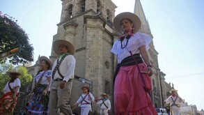 Personas caracterizadas de adelitas y revolucionarios caminando frente a la Catedral de Guadalajara en desfile de la Revolución Mexicana