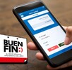 Mano sosteniendo un teléfono celular con una aplicación bancaria abierta y una mesa de madera de fondo. El logo del Buen Fin en la esquina inferior inzquierda