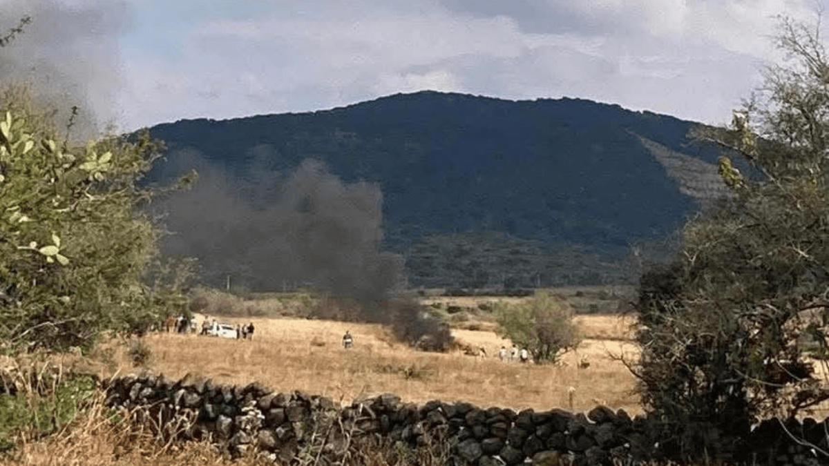 Avioneta caída en campo abierto. Una vista de un amplio campo seco rodeado de arbustos y con una colina oscura en el fondo.