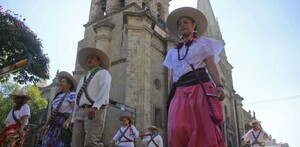 Personas caracterizadas de adelitas y revolucionarios caminando frente a la Catedral de Guadalajara en desfile de la Revolución Mexicana