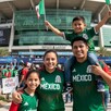 Familia mexicana vistiendo playeras de la Selección Mexicana a las afueras del Estadio Akron en Guadalajara con multitud de personas de fondo