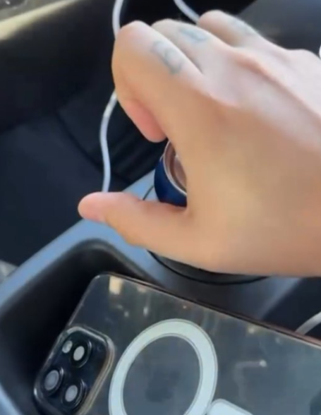 Mano de 'El Jerry' tomando una lata de cerveza en el portavasos de un auto con un iPhone a un lado.