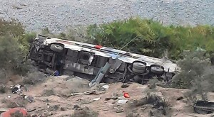 Autobús volcado sobre matorrales y tierra luego de caer desde un precipicio con diversos objetos esparcidos alrededor