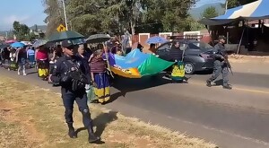Habitantes de la localidad de Santa Fe de la Laguna caminando por las calles en caravana fúnebre con dos oficiales de policía escoltándolos al frente