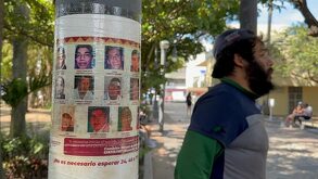 Un hombre de gorra y barba junto a un poste que tiene pegadas las fotografías de personas desaparecidas en Veracruz.