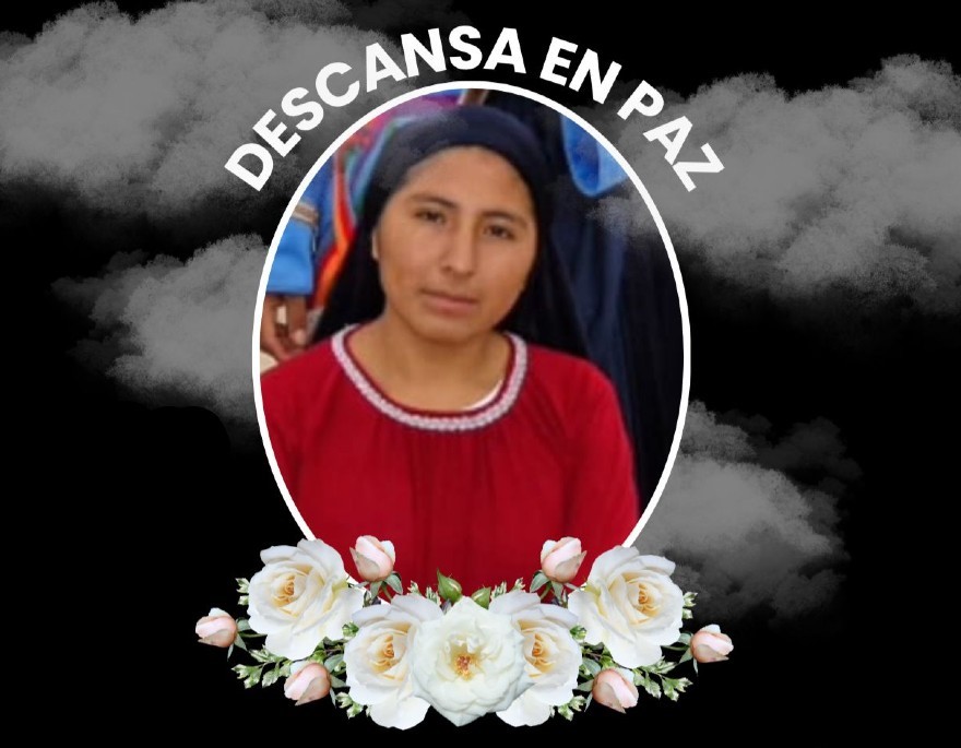 Imagen de Rebeca Apaza Arcos viendo de frente y vistiendo una blusa roja con un poncho negro sobre la cabeza. Flores blancas bajo la foto y fondo negro.