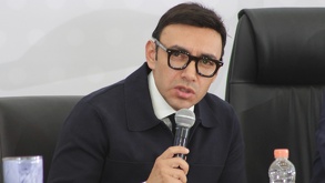 Hombre con lentes grandes hablando ante un micrófono.