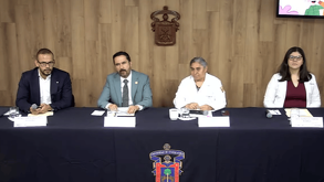 Cuatro funcionarios (dos hombres y dos mujeres, una de ellas en bata médica) sentados en una mesa de conferencia con el escudo de la Universidad de Guadalajara